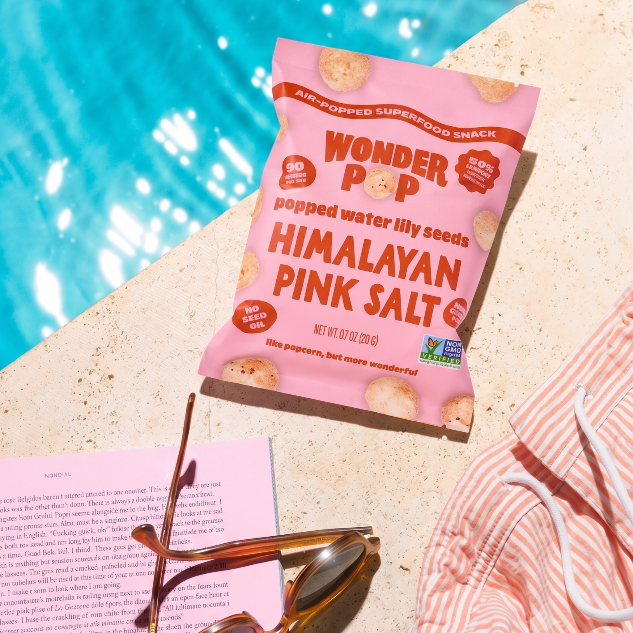 Pink package of Wonder Pop Himalayan Pink Salt snack by a poolside with sunglasses and a book.