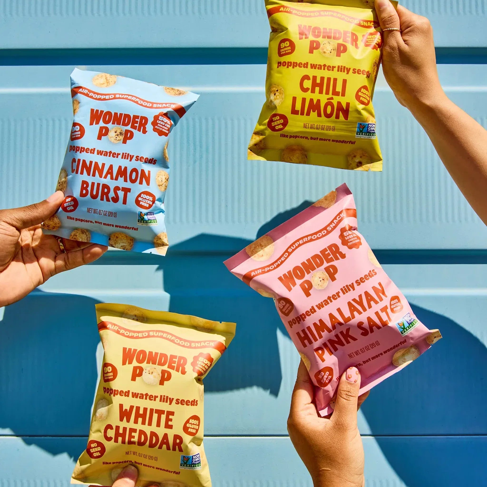 Four Wonder Pop snack bags in different flavors held by hands against a blue background