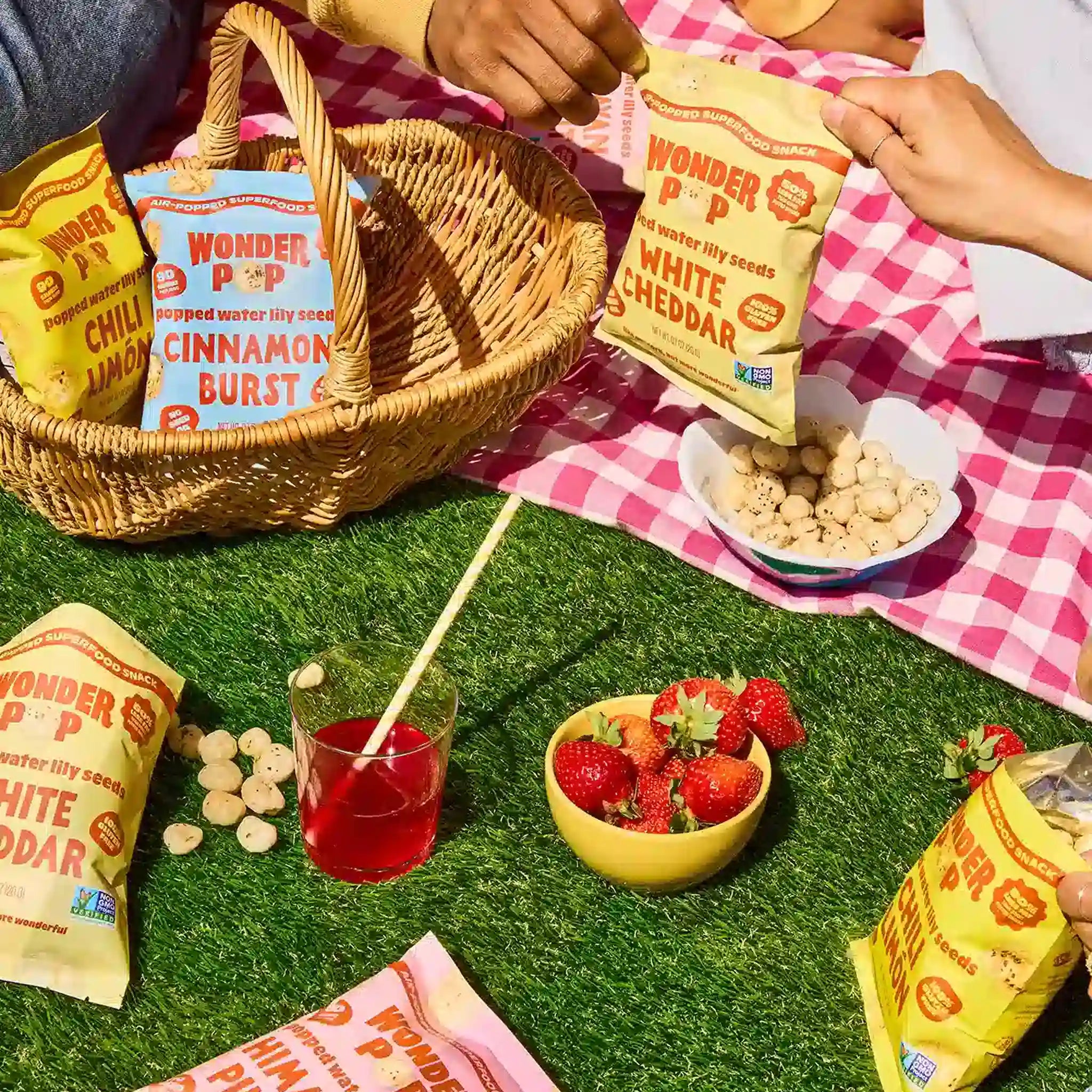 Picnic scene with Wonder Pop bags, strawberries, and a basket on a checkered blanket.