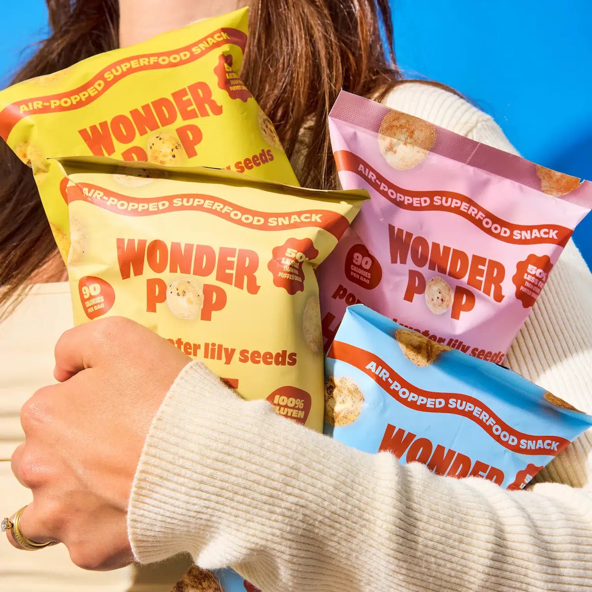 Person holding multiple Wonder Pop snack packages against a blue background